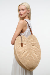 Natural raffia palm leaf tote bag worn with brown leather shoulder straps