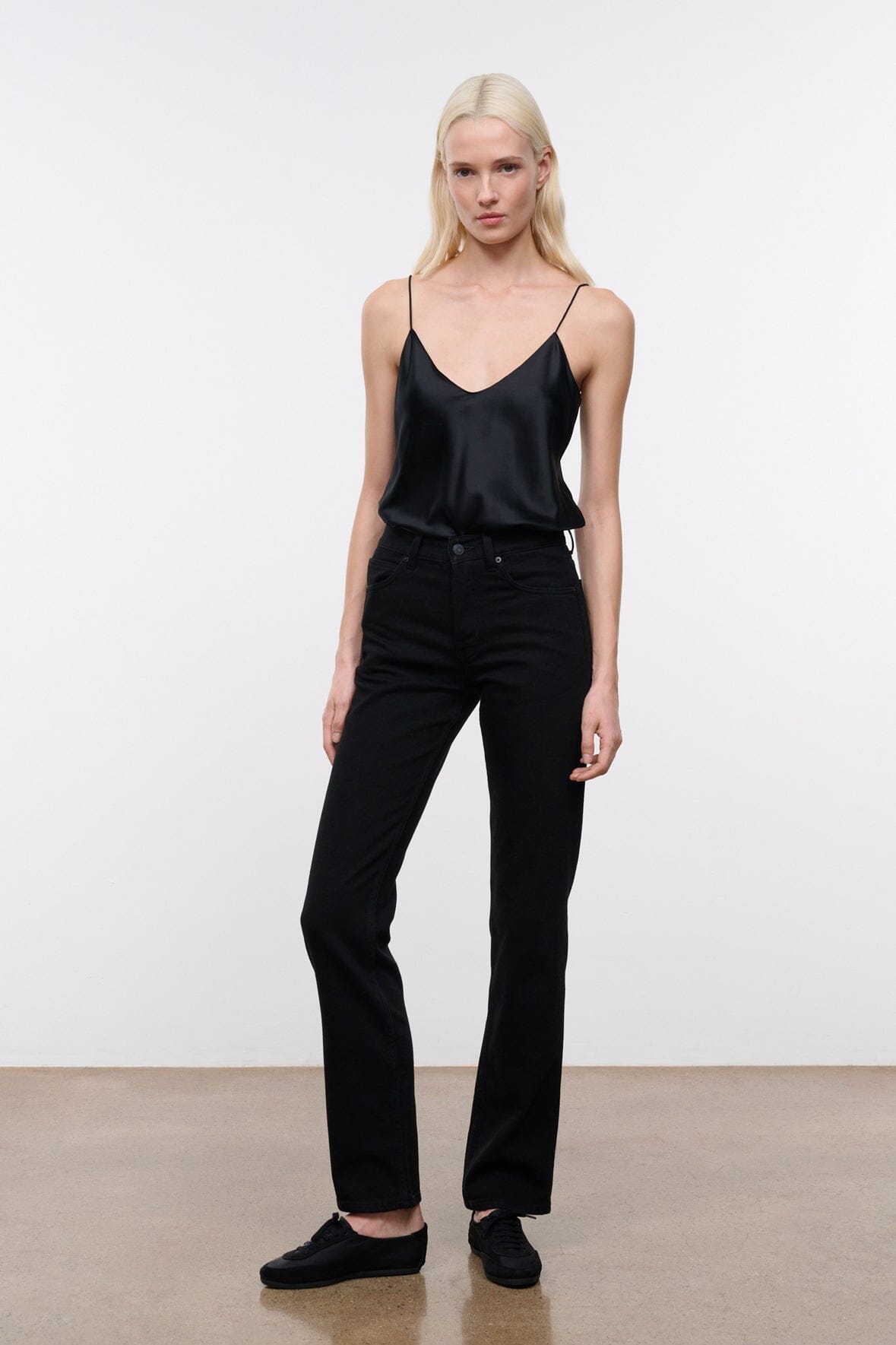 Black straight jeans on model, with front button fly, belt loops, and stacked seams